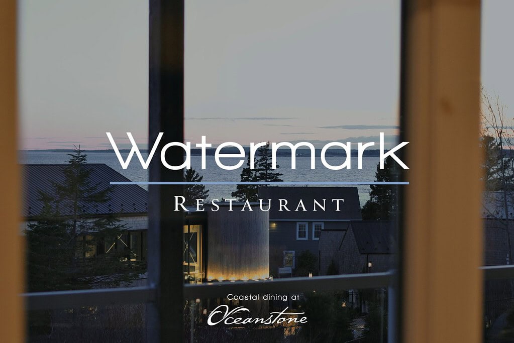 A tranquil dusk view through a window at Oceanstone Resort, overlooking trees and ocean, with Watermark Restaurant’s logo visible.
