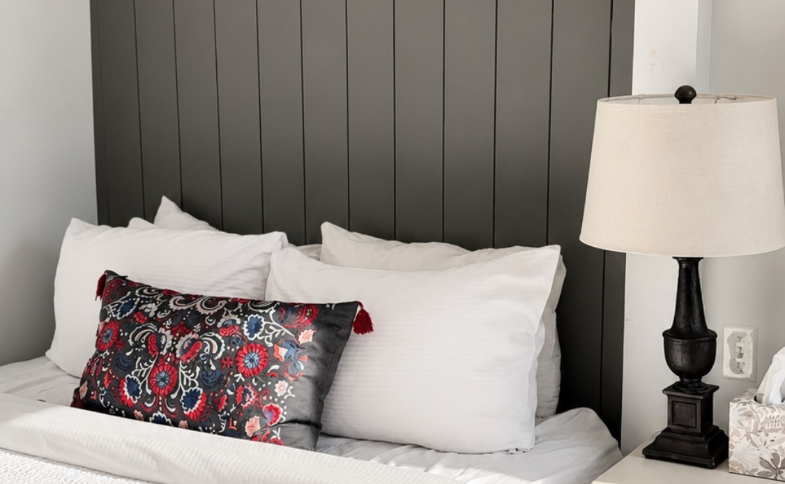 17 A serene bed with crisp white linens and soft pillows rests by a paneled headboard; warm light glows from a bedside lamp.